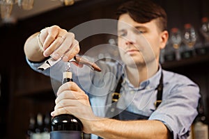 Male sommelier open wine bottle with corkscrew.