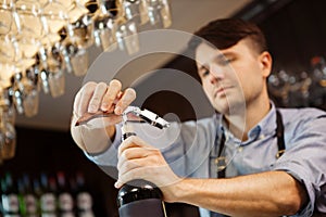 Male sommelier open wine bottle with corkscrew.