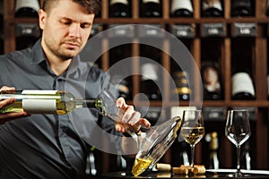 Male sommelier pouring white wine in decanter