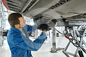 Male specialist repairing the equipment under car in garage