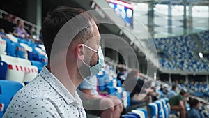 Male spectator in a medical mask in profile watching a match at the stadium