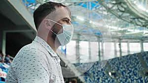 Male spectator on a stadium in medical mask rubs his hands with sanitizer
