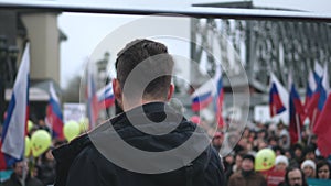 Male spokesperson on stage with mic gives address to crowd with Russian banners.