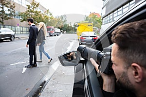 Male Spy Taking Photograph Of A Couple Walking On Street