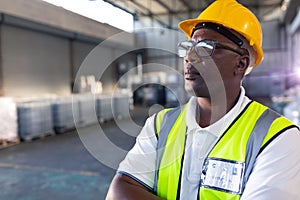 Male staff in hardhat and reflective jacket standing with arms crossed in warehouse