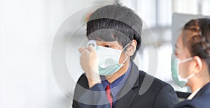 Male staff wearing medical face mask is checking fever by his colleague using infrared thermometer