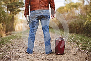 Male standing on an empty pathway near his old suitcase while hiding the bible
