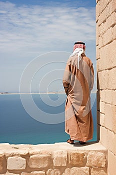 Male standing on the shoreline, facing the vast ocean, wearing a warm, brown robe. Ai generated
