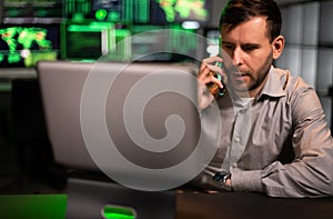 Male stock market trader working in office using laptop and talking on mobile phone with client.