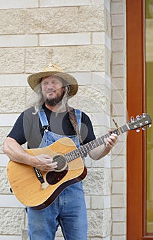 Male street performer wearing a sun hat playing guitar