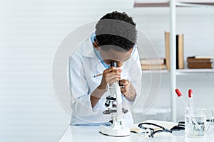 Male student of African descent schoolgirl in science classroom doing chemistry experiment. male student using microscope Look at