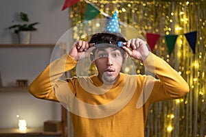 Male student on his birthday have negative news, touching his glasses, being mad, upset and surprised standing at home