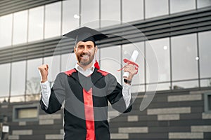 Male student holding diploma, smiling, showing hurray.