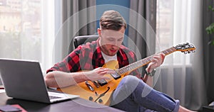 A male student is learning to play the electric guitar. A young boy reviews a