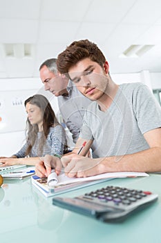 Male student making notes calculator in foreground