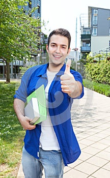 Male student with paperwork on campus showing thumb up