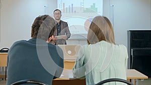 Male student raising hand and asking teacher a question sitting on table