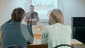 Male student raising hand and asking teacher a question sitting on table