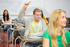 Male student raising hand by others in classroom