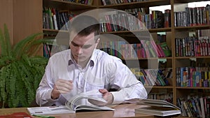 Male student researching with a book in a library