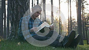 Male student sitting on grass in public park and reading book at beautiful sunset. Portrait of young student study in park and rea