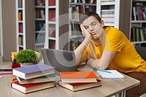 Male student sleeping at workplace in college library