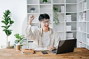 Male student taking notes from a book at library, Young asian sitting at desk doing assignments in college library