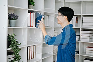 Male student taking notes from a book at library, Young asian sitting at desk doing assignments in college library