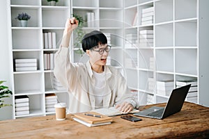 Male student taking notes from a book at library, Young asian sitting at desk doing assignments in college library