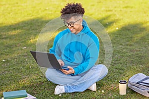 Male student working on laptop in grassy field photo