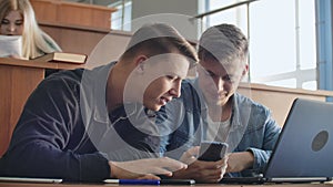 Male students with a smartphone in their hands laughing in the audience during a break for a lecture at the University