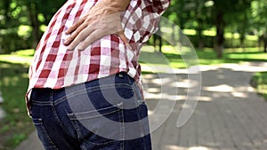 Male suffering back ache discomfort, walking in park, health care, rheumatism