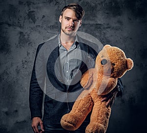 Male in a suit holding brown teddy bear.