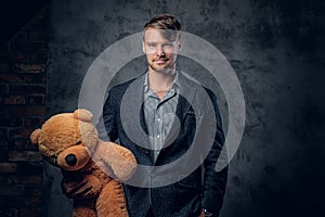 Male in a suit holding brown teddy bear.