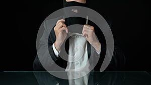 Male in suit putting on balaclava, government corruption, black background