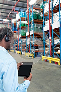 Male supervisor with headset using digital tablet in warehouse