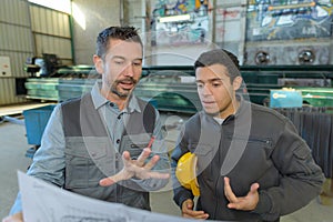 Male supervisor with workers discussing over blueprints in industry