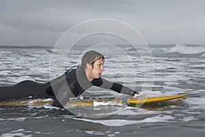 Male Surfer Paddling On Surfboard In Water At Beach