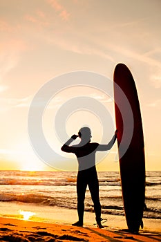 Male surfer silhouette with yellow longboard on a ocean coast at sunset. Water sport adventure camp and extreme swim on summer