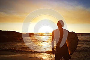 Male surfer watching the sunset at the beach