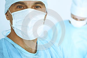 A male surgeon headshot, a group of surgeons is operating in the background. Health care concept