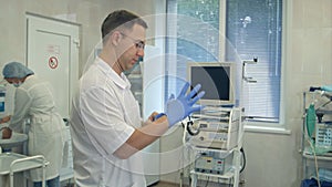 Male surgeon putting on sterile rubber gloves for surgery while nurse washing her hands in a surgery room