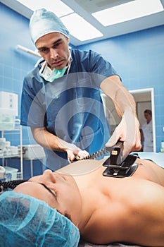 Male surgeon resuscitating an unconscious patient with a defibrillator