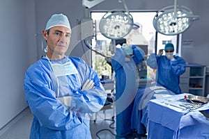 Male surgeon standing with arm crossed in operation room while surgeons getting ready for operation