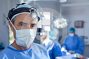 Male surgeon with surgical headlight standing in operation room