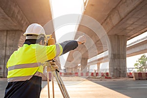 A male surveyor engineers worker making measuring and pointing finger with theodolite on road works. Survey engineer at road