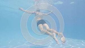Male swimmer diving under blue water swimming pool. Underwater view young man jumping in transparent swimming pool
