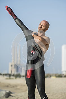 Male swimmer getting ready for swim training in the beach with urban background. Confident man putting on a wetsuit to