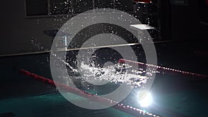 Male swimmer jumps off starting block and start swims in pool. Professional athlete training: dive and splashes water