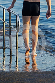 Male swimmer walking toward the sea holding the pier fence at sunset